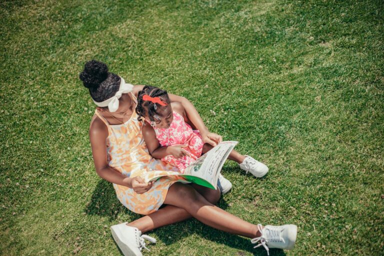 african american girls reading book on grass